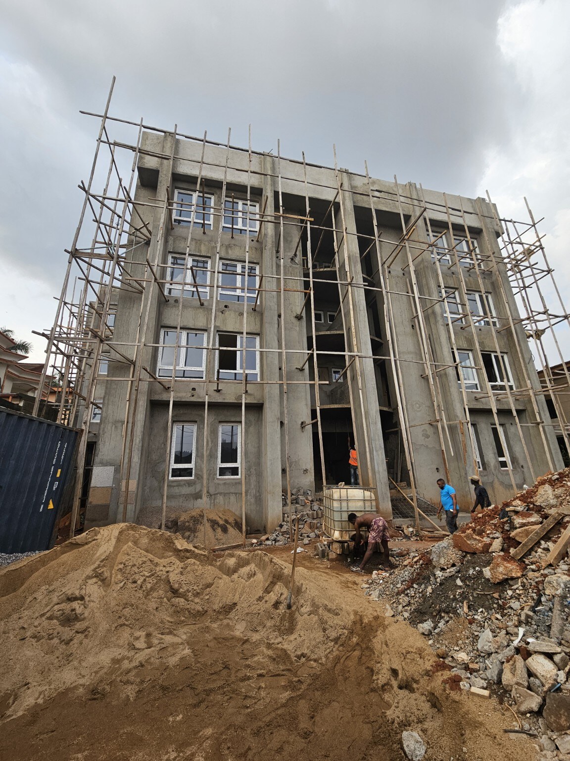 Front façade of Golf Residences under construction with windows installed, exterior finish work underway, and workers at the entrance.